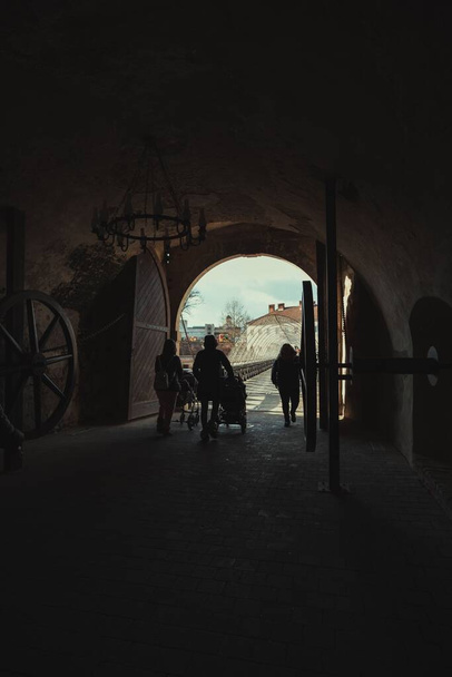 A vertical shot of people crossing the dark covered passageway to the city - Valokuva, kuva