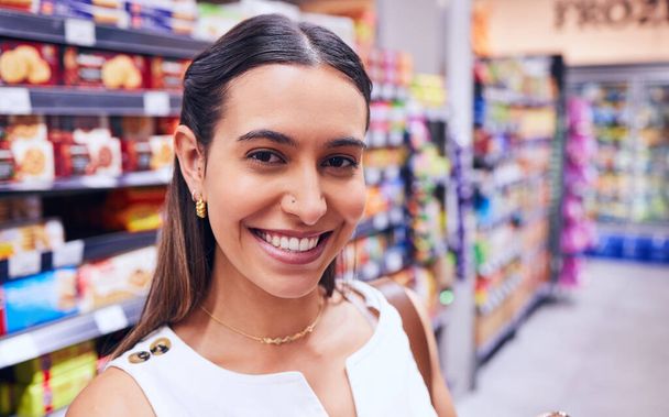 Shopping, groceries and consumerism with a young woman in a grocery store, retail shop or supermarket aisle. Closeup portrait of a female standing with packed shelves of consumables in the background. - Foto, Bild