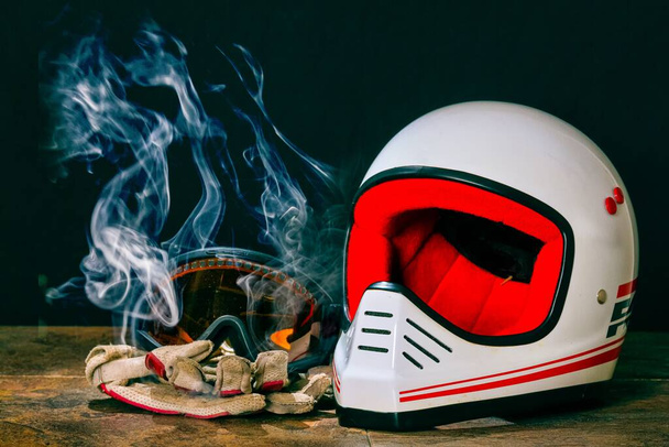 A closeup of a helmet, goggles, and gloves on a table with smoke. - Фото, изображение