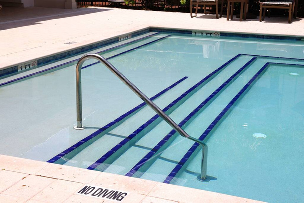 The metal handrail with stairs at the pool with clean cold water. Text: no diving. - Photo, Image