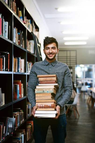 Ready to ace that assignment. Portrait of a happy young man carrying books in a library at college - Φωτογραφία, εικόνα