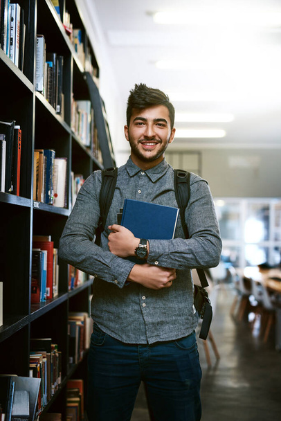 Total dedication to his education. Portrait of a happy young man carrying books in a library at college - Foto, afbeelding