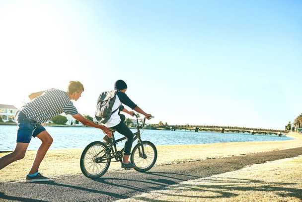 Дай йому поштовх. молодий хлопчик навчає свого молодшого брата їздити на велосипеді поруч з лагуною
 - Фото, зображення