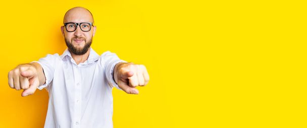 Smiling young man pointing fingers at viewer on yellow background. Banner. - 写真・画像