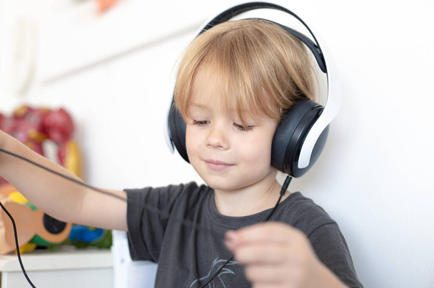 Κοντινό πορτραίτο μικρού χαρούμενου αγοριού με ακουστικά που ακούει μουσική στο δωμάτιό του. - Φωτογραφία, εικόνα