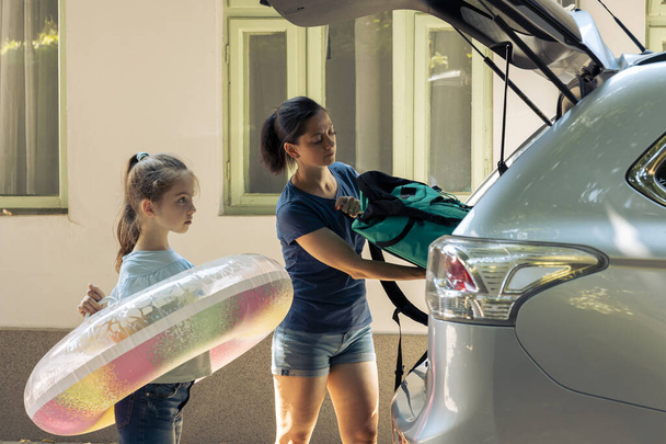 Mother with kid loading baggage in trunk, preparing to leave on road trip journey. Woman and small child travelling on holiday vacation at seaside during summer, happy recreation. - Photo, image