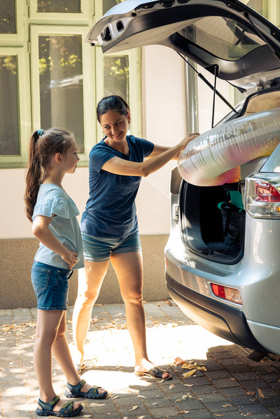 Small family leaving on holiday road trip with inflatable and baggage in automobile trunk. Mother with young kid going on summer vacation at seaside. Going on journey adventure with vehicle. - Foto, Imagen