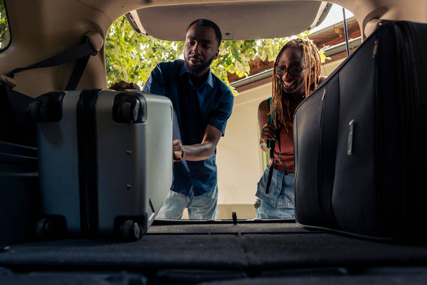 Man and woman loading baggage in vehicle trunk, leaving on summer holiday together. Couple preparing car with travel bags and luggage to go on vacation trip and drive to destination. - Photo, image