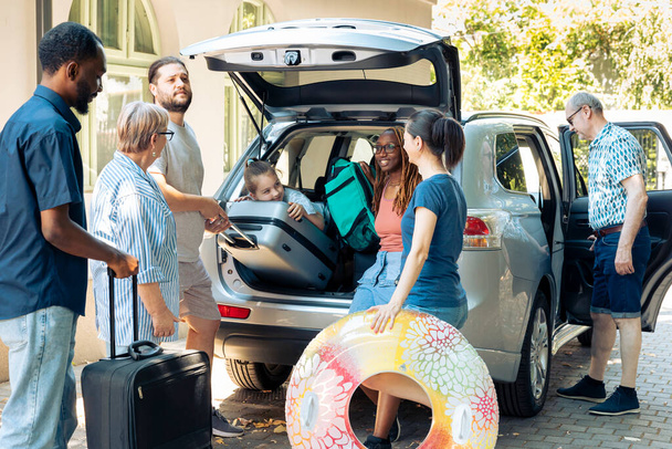 Mixed family and friends going on holiday, preparing vehicle with bags and luggage to go on summer vacation. Multiethnic people travelling on journey adventure with baggage in automobile. - Foto, Imagen