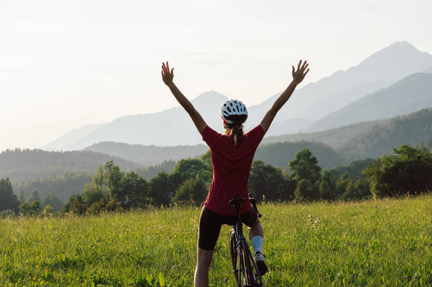 Happy female road racing cyclist in joy, with arms raised above her head, after successfully reaching a goal - Фото, изображение