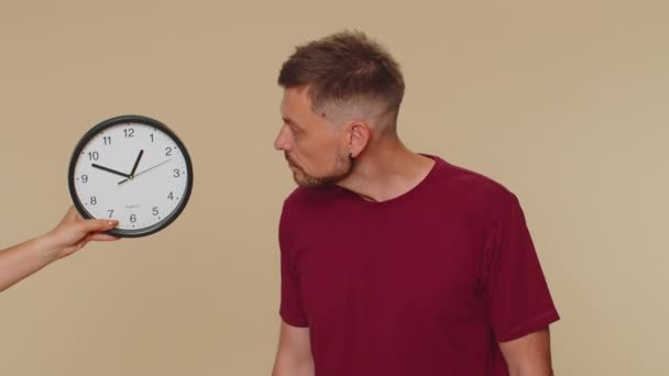 Confused young man in red t-shirt with anxiety checking time on clock, running late to work, being in delay, deadline. Adult stylish male guy looking at hour, minutes, worrying to be punctual, indoors - Imágenes, Vídeo