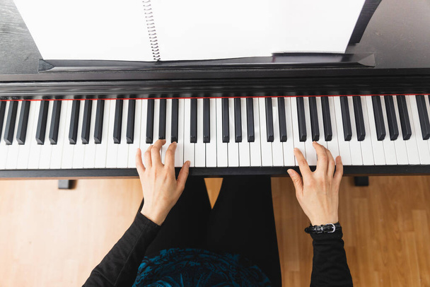 Вид зверху на жіночі руки, що грають на піаніно, читаючи ноти. Високоякісна фотографія
 - Фото, зображення