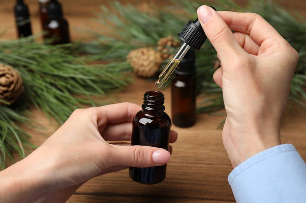 Woman holding pipette with pine essential oil over bottle at wooden table, closeup - Foto, Imagen