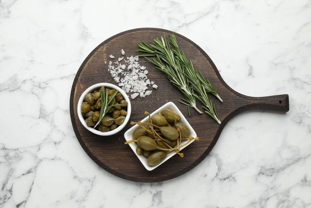Delicious pickled capers, salt and rosemary twigs on white marble table, top view - Fotoğraf, Görsel