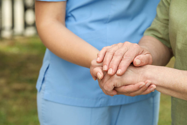 Elderly woman and female caregiver holding hands outdoors, closeup - Fotó, kép