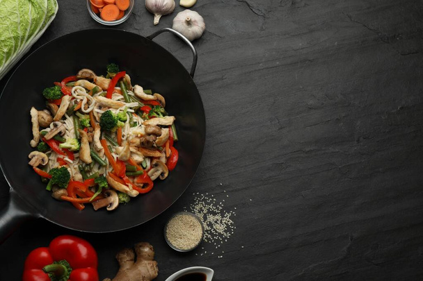 Stir fried noodles with mushrooms, chicken and vegetables in wok on black table, flat lay. Space for text - Фото, зображення