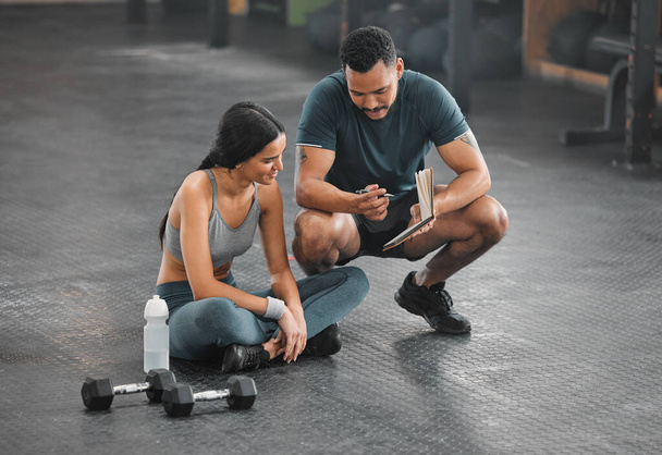 Personal trainer, coach or fitness instructor helping an active and fit woman in the gym. Young female athlete sitting down and managing her workout routine or schedule with her exercising partner. - Photo, image