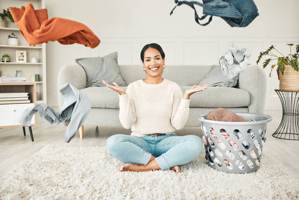 Portrait of a cleaning, carefree female cleaner throwing clothing in the air. Happy, smiling and young woman doing laundry, washing clothes and sitting in a messy living room at home - Фото, зображення