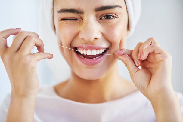 Go the extra mile for your smile. Portrait of a beautiful young woman flossing her teeth in the bathroom at home - Foto, Imagen
