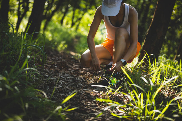 Woman runner tying shoelace on forest trail - 写真・画像
