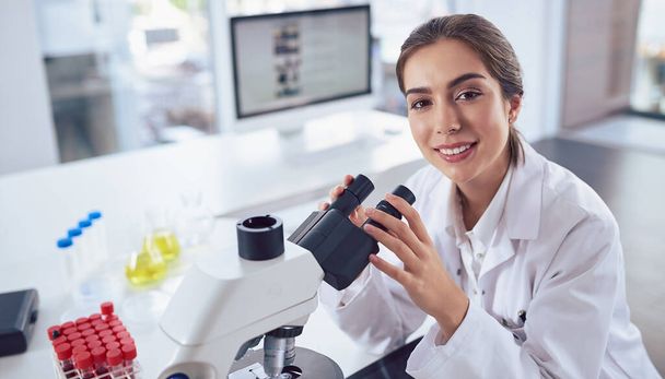 Scientists always have the most state of the art equipment. Portrait of a cheerful young female scientist using a microscope while looking at the camera inside of a laboratory - Fotó, kép