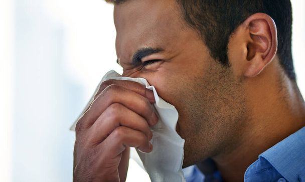 Struggling to fend off the flu this season. a young businessman blowing his nose at work - 写真・画像
