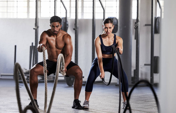 Active, fitness partners training together, exercising with battle ropes in gym. Athletic sports couple in motion doing arms and cardio workout in wellness center for strength and healthy lifestyle - 写真・画像