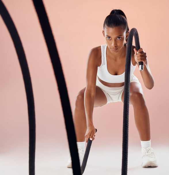 Fitness, battle ropes and active woman in a routine workout, training and exercise against pink studio background. Sporty, athletic and strong athlete exercising for cardio health and muscle strength. - 写真・画像