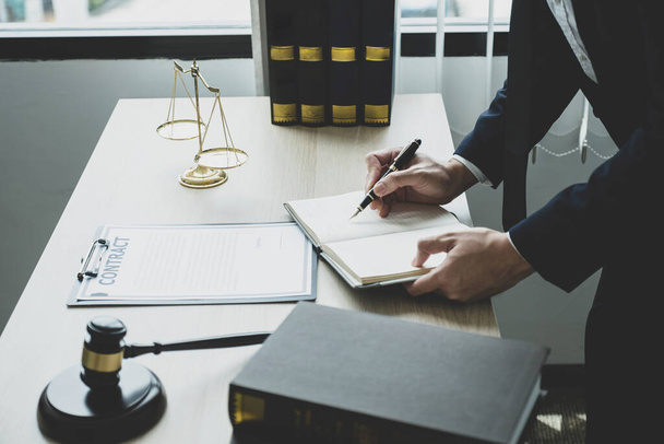 Адвокат держит ручку в руках и предоставляет юридическую консультацию по вопросам ведения бизнеса в офисе с помощью шкалы правосудия и молотка. - Фото, изображение