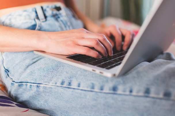 Una chica trabaja desde casa, las manos femeninas en un teclado portátil de cerca, una mujer se sienta en un sofá con un ordenador portátil - Foto, imagen