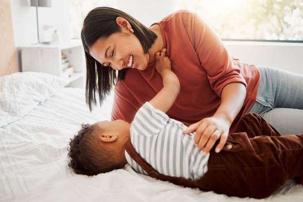 Happy, loving family with a mother and son being playful and bonding on a bed at home. Smiling parent playing with her child, laughing and enjoying motherhood. Single parent embracing her son. - Photo, image