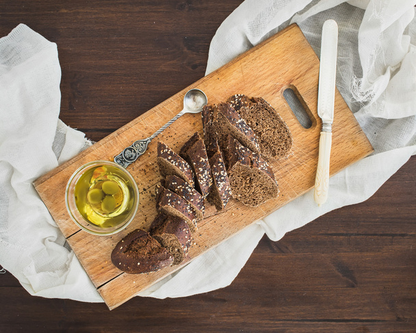 Dark baguette cut in slices with olive oil on a rustic wooden bo - Fotoğraf, Görsel