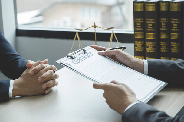 Lawyer hand holding pen and providing legal consult business dispute service to the man at the office with justice scale and gavel hammer. - Foto, afbeelding