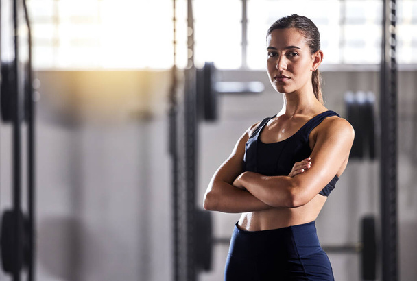 Fit, slim and serious woman with arms crossed, feeling confident about her body and health while standing in gym. Portrait of a sporty and determined woman ready to exercise to stay in healthy shape. - Photo, image