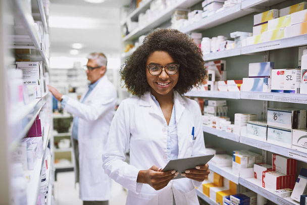 Medication for everyone. Portrait of a cheerful young female pharmacist holding a digital tablet while looking at the camera in a pharmacy - Foto, immagini