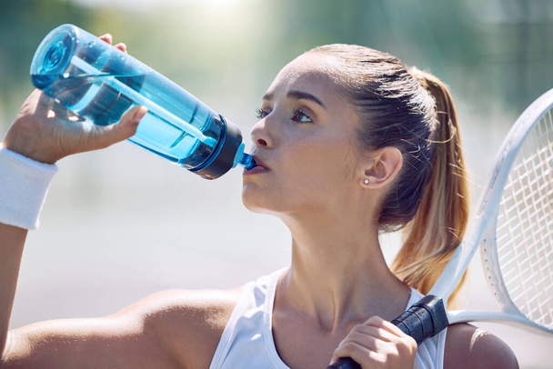 Υγεία, φυσική κατάσταση και νερό, μια γυναίκα τενίστρια σε ένα διάλειμμα, πίνοντας από ένα πλαστικό μπουκάλι κατά τη διάρκεια ενός αγώνα στο γήπεδο. Όμορφη νεαρή κοπέλα που παίζει σπορ, προπόνηση για έναν υγιεινό καλοκαιρινό τρόπο ζωής - Φωτογραφία, εικόνα