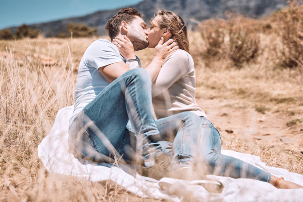 Kissing, in love and young couple on picnic valentine date outdoors in sunny summer or spring. Intimate, passionate and dating romantic cute boyfriend and girlfriend in relationship together outside - Photo, image