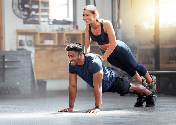 Fitness, strong and wellness couple exercising, training or workout exercise inside gym. Sporty professional woman and man or trainer doing pushup and balance in a physical endurance session. - Foto, afbeelding