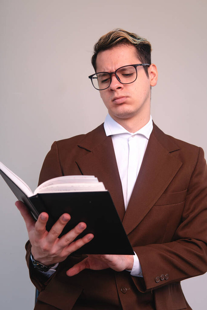 Заплутаний елегантний чоловік уважно читає книгу. Чоловік у костюмі, сорочці та окулярах вчиться. Досвідчений чоловік читає чорну книгу. Бізнесмен уважно аналізує свою книгу. Високоякісна фотографія
 - Фото, зображення