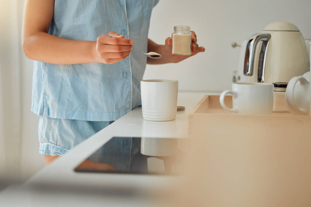 Casual woman adding sugar while preparing a cup of coffee, tea or hot chocolate in the kitchen during the morning. Female hands holding teaspoon for a fresh beverage in a mug for breakfast at home. - Foto, immagini