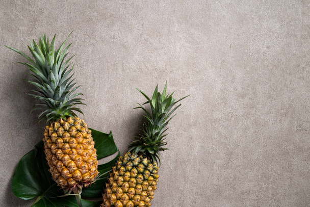 Top view of fresh pineapple with tropical monstera leaves on gray background. - Fotó, kép