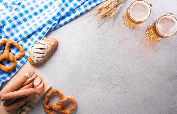 Oktoberfest festival decoration symbols made from Pretzel loaf, beer, sausage, potato chips and Bavarian white and blue fabric on stone background. - 写真・画像