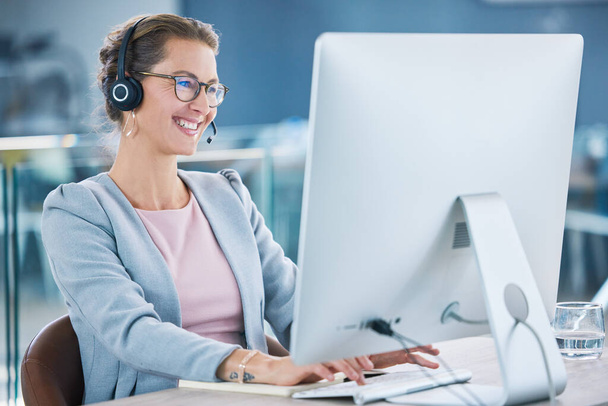 Call center, customer service and agent with computer talking to customers, helping and answering office calls. Mature, happy and friendly helpdesk operator, secretary and contact us client support. - Foto, Imagen