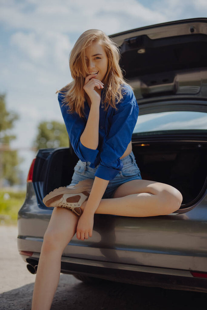 Happy funny young woman tourist sitting on the car at the road trip - 写真・画像