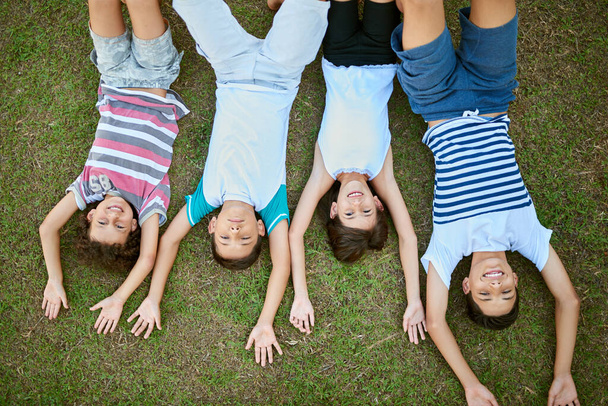 Who better to share a childhood with than siblings. High angle portrait of a group of happy siblings lying together on the grass - Fotoğraf, Görsel
