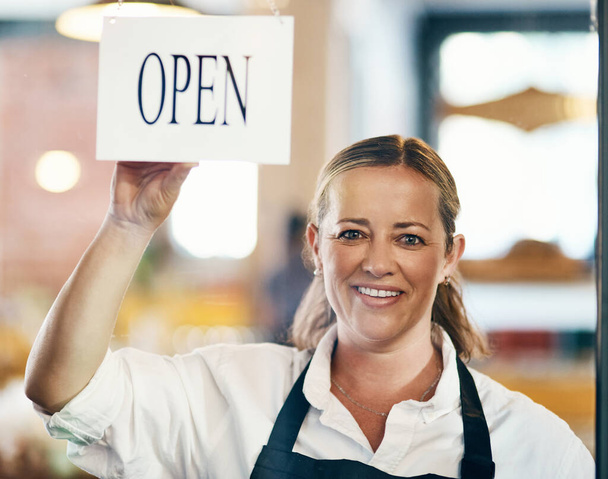 Cafe owner opening her new startup, store or welcoming customers to a restaurant. Caucasian manager reopening her business after closing down. Waitress holding open sign at window or entrance - Zdjęcie, obraz