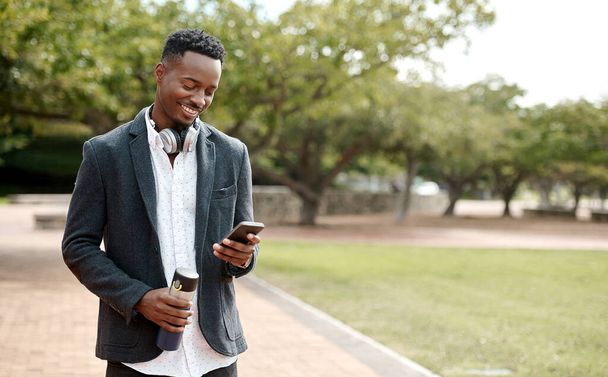 Young, cool smiling businessman on a phone having a walk in the park outside in nature. Happy man texting, chatting or reading messages on a smartphone outdoors on a break from work, over copy space - Fotografie, Obrázek
