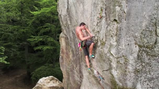 Young man climber climbing difficult route on a high rock with rope. Fearless rock climber training rock climbing on summer day. Concept of extreme sport, adventures and active lifestyle. Aerial view. - Footage, Video