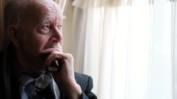 Close up portrait of a lonely old man, an elderly man of an elderly grandfather sitting by the window, feeling pain and in need of help, a depressed pensioner - Felvétel, videó