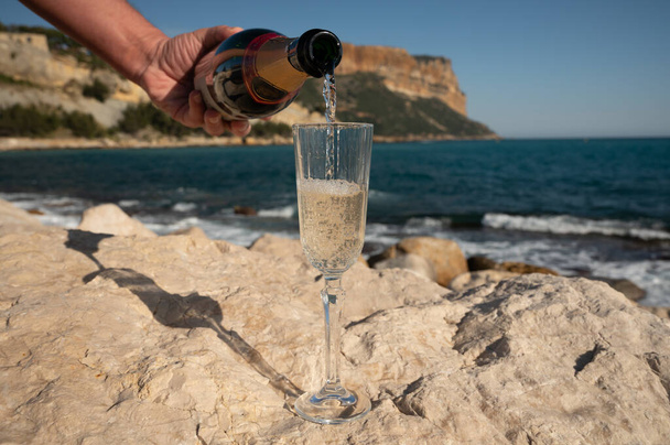 Fransız şampanyası bardakta köpüklü şarap ve kumsalın manzarası, Cassis, Provence, Fransa 'da mavi deniz suyu ve dağlar - Fotoğraf, Görsel